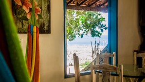 A room with a view of a beach through a window, a wooden chair, and a painting on the wall. - Ankh Jeri (Jijoca de Jericoacoara)