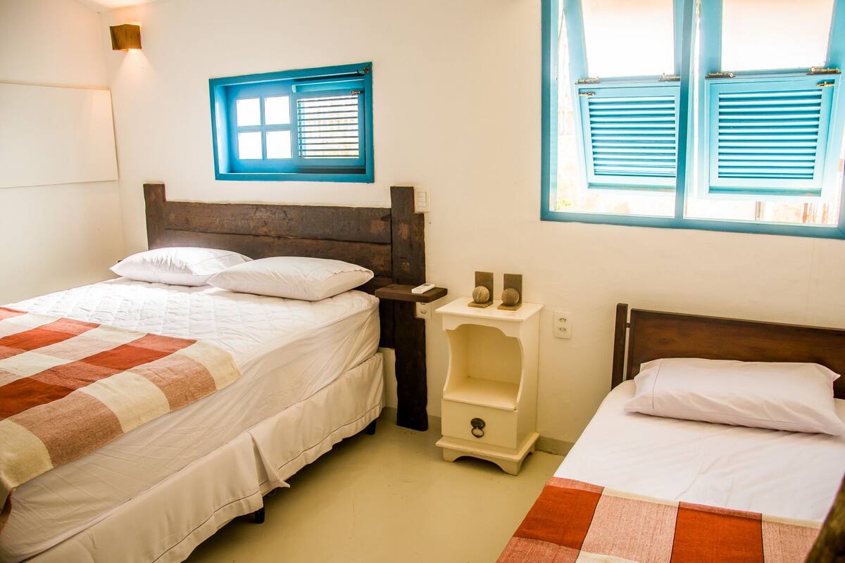 Une chambre avec deux lits, une table de chevet, une petite étagère et une fenêtre avec des volets.