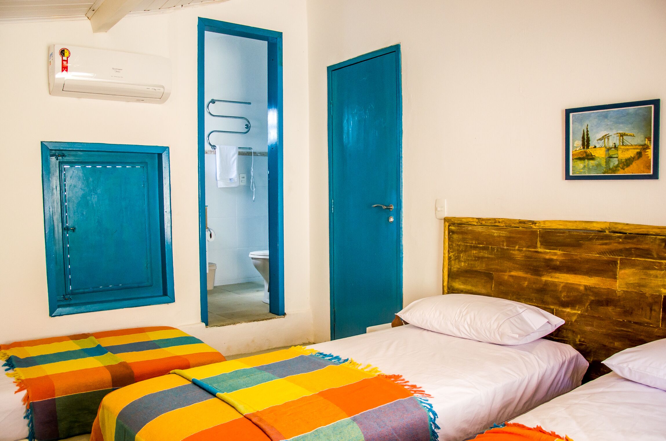 Une chambre avec deux lits, une salle de bain visible à travers une porte ouverte et un tableau accroché au mur.