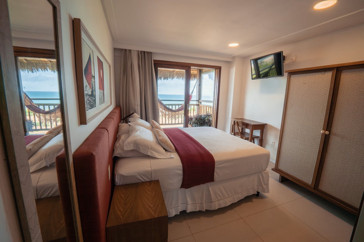 Une chambre d’hôtel avec un lit, une télévision, une armoire et un balcon donnant sur la mer.