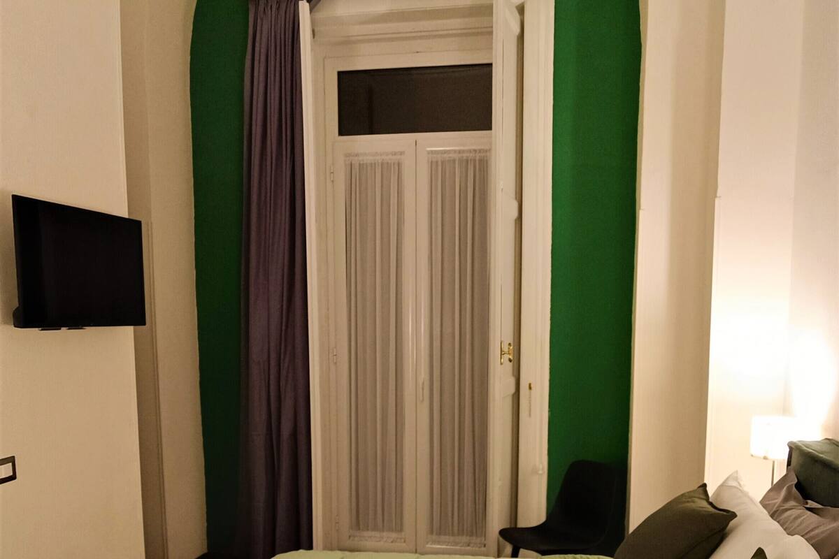 Una habitación con una cama, un televisor montado en la pared, una puerta con cortinas y una pared verde.