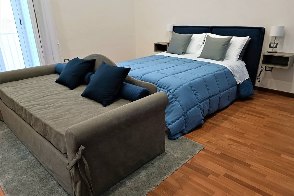 Un dormitorio con cama, sofá, mesita de noche y lámpara.