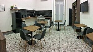 Uma cozinha compacta com geladeira preta, micro-ondas e pia, além de um espaço de refeições com quatro mesas e cadeiras.