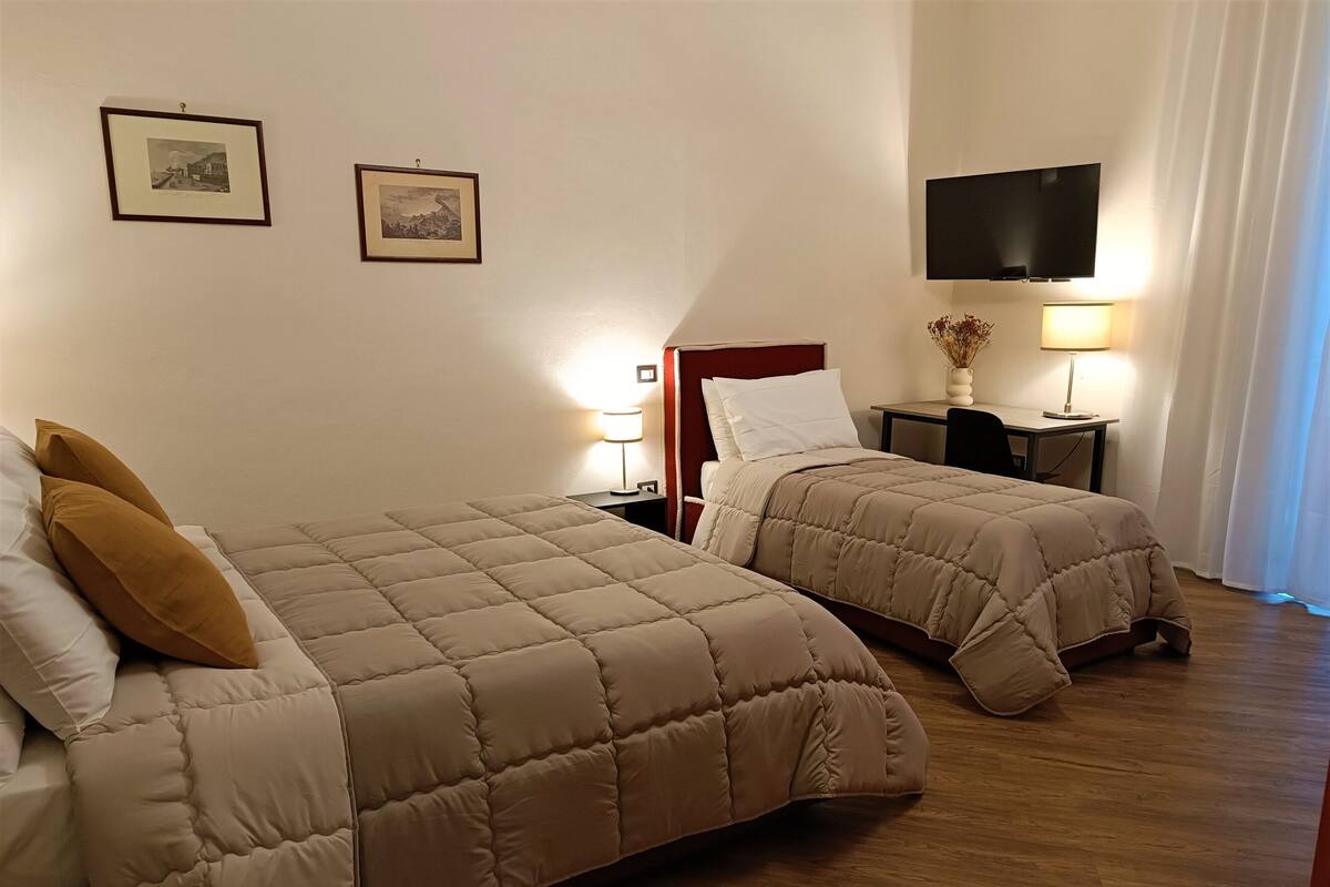 Habitación de hotel con dos camas, un televisor montado en la pared y un escritorio con lámpara.