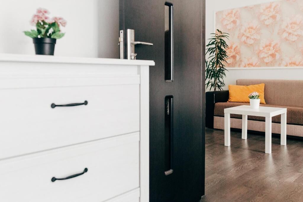 Una habitación moderna con un aparador blanco, una puerta negra, un sofá marrón y una mesa de centro blanca, además de un cuadro floral en la pared.