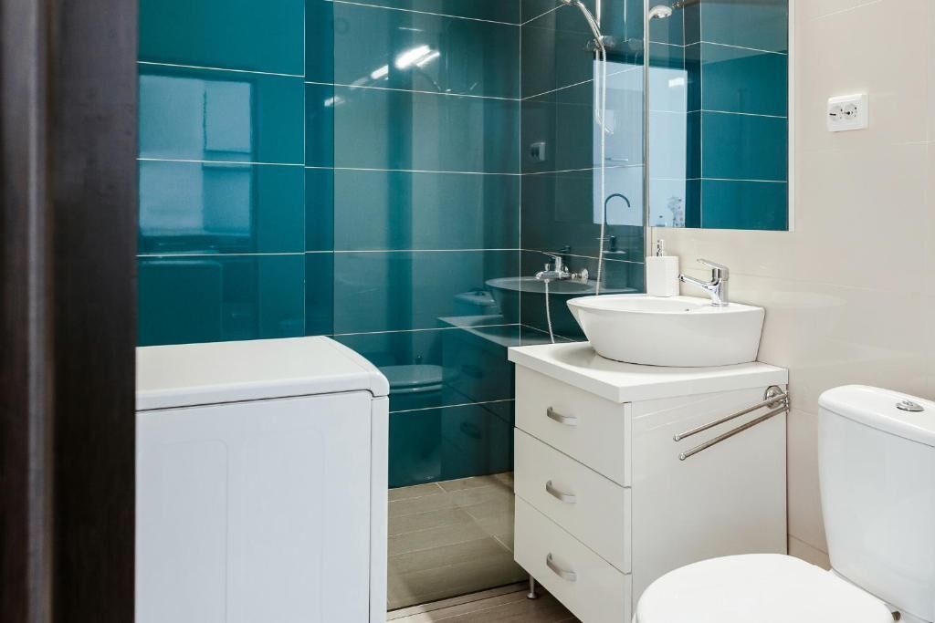 Un baño moderno con azulejos verde mar, un lavamanos blanco y un inodoro.