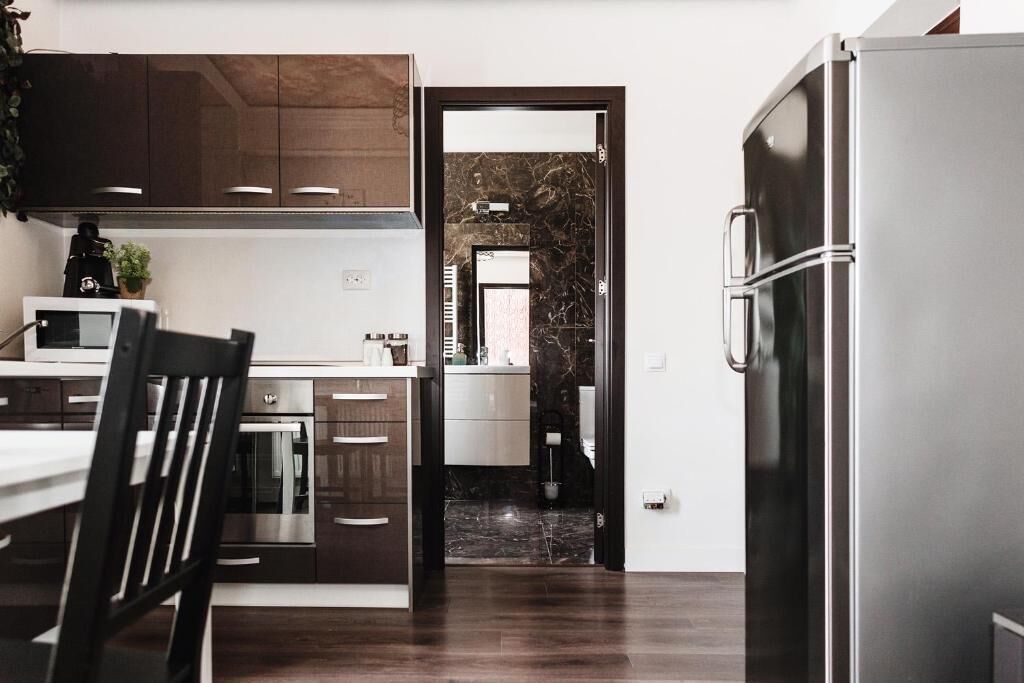 A modern kitchen with dark wooden cabinets, a stainless steel refrigerator, and a marble backsplash.