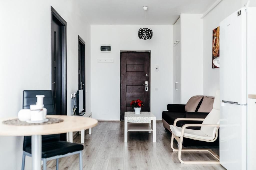 A modern living room with a dark wooden door, a white sofa, a small table with a vase, and a white refrigerator.