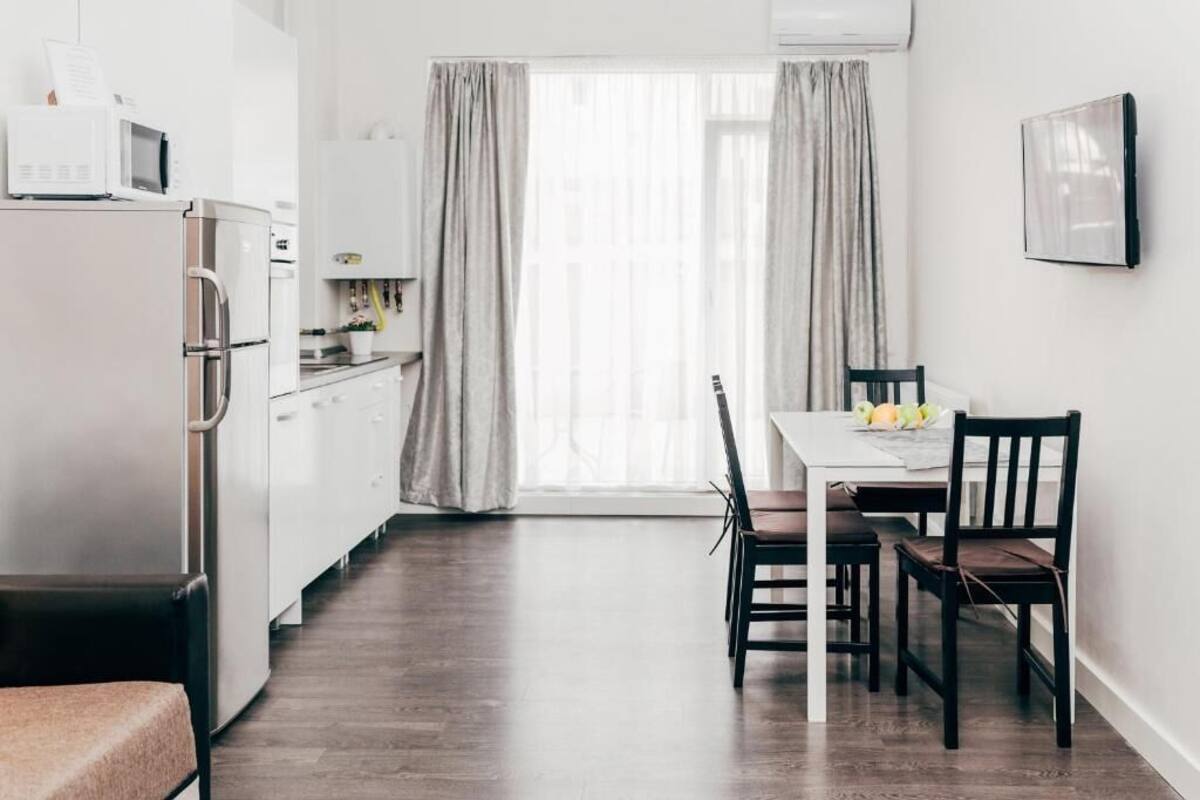 A compact kitchen with a refrigerator, microwave, and stove, a dining table with chairs, and a window with curtains.
