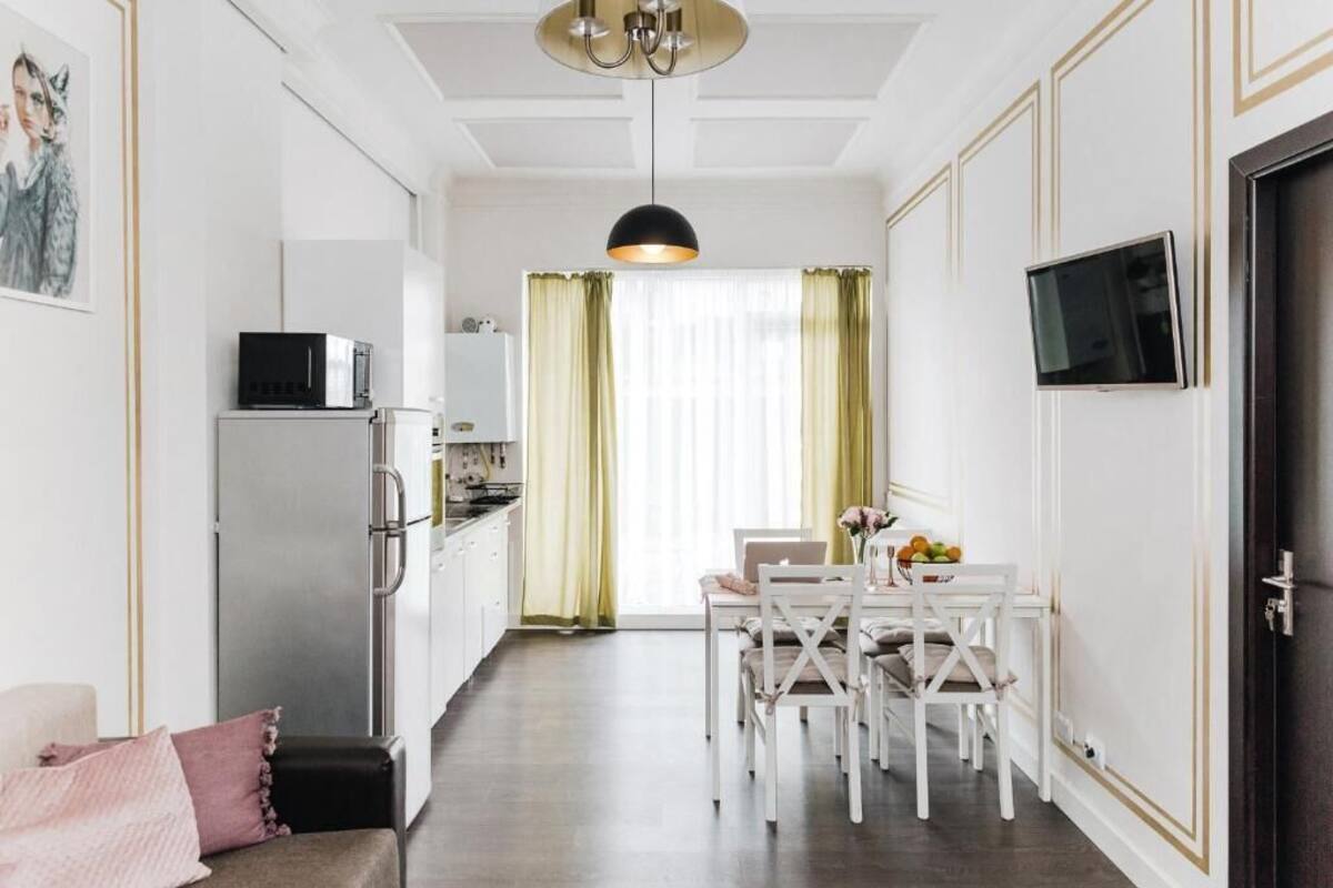 A modern kitchen with a dining area, white cabinetry, and a flat-screen TV mounted on the wall.