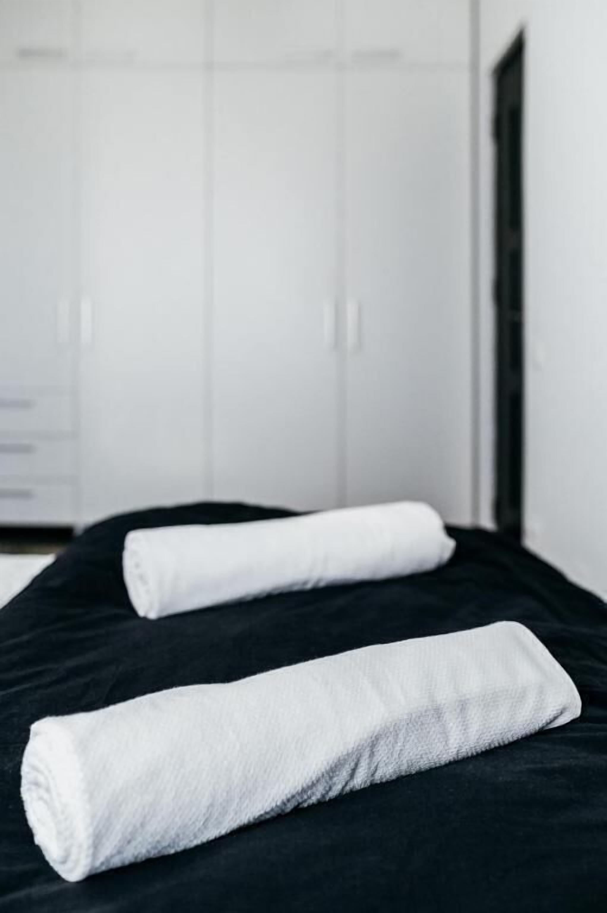 A bed with two white towels and a black bedspread in a room with white walls and a door.