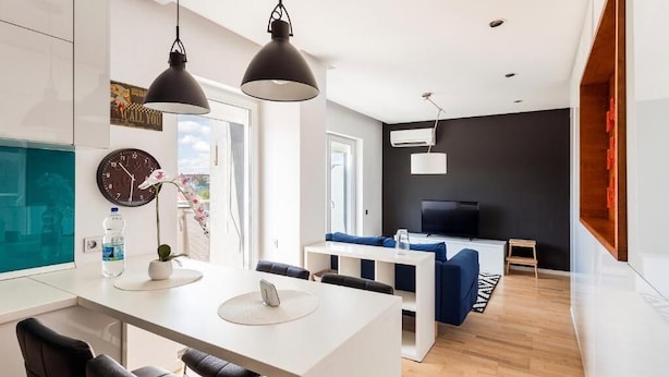 A modern living room with a white sofa, a TV, and a dining area with a white table and chairs. - DD Apartments (Cluj-Napoca)