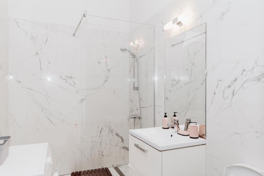 A modern bathroom with a glass shower enclosure, white marble walls, and a vanity with a mirror.