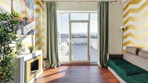 A living room with a sofa, a fireplace, and a view of the city through large windows. - DD Apartments (Cluj-Napoca)