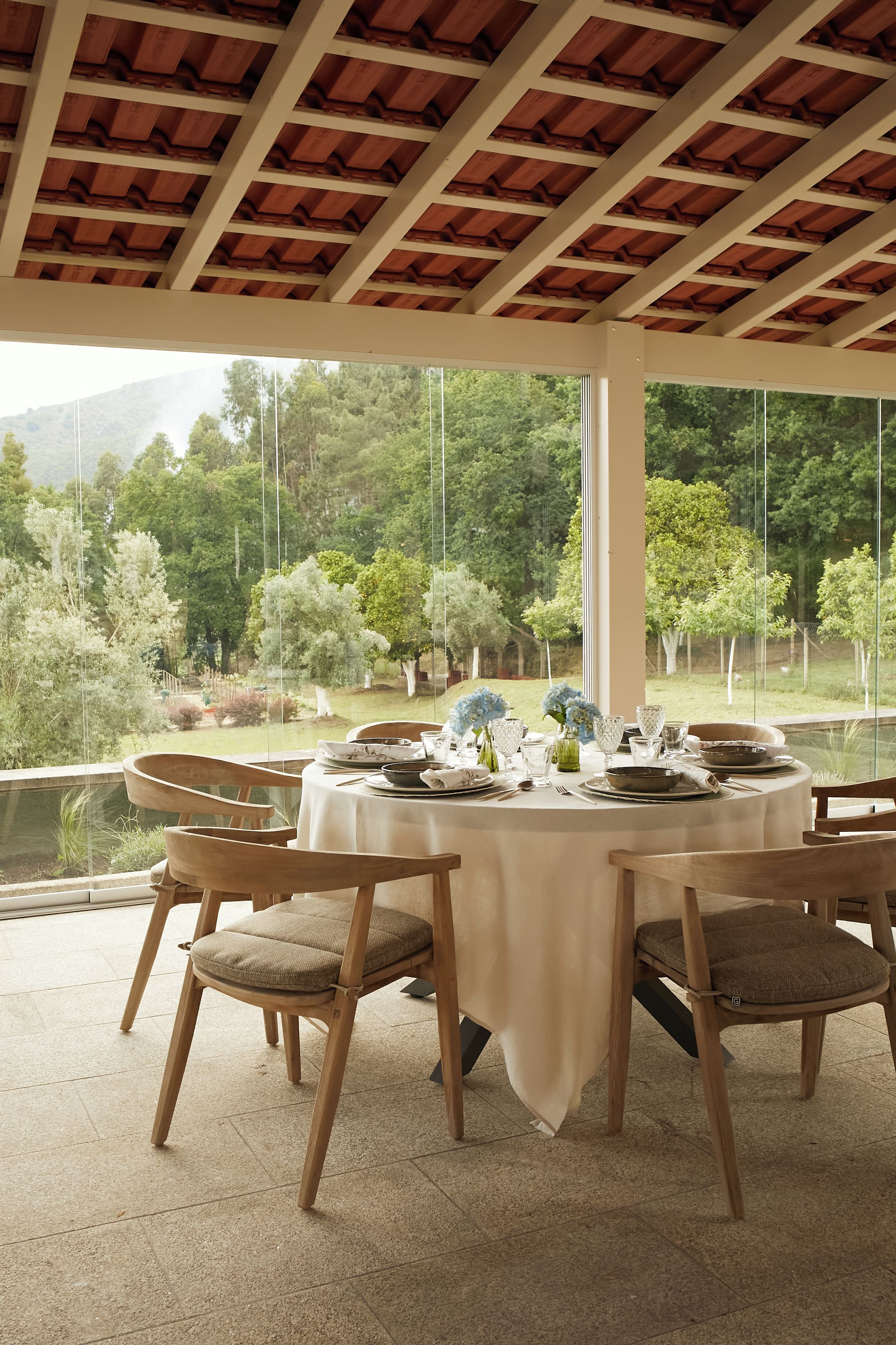 Una mesa redonda lista para comer, con sillas, vista a un jardín y una estructura de pérgola.