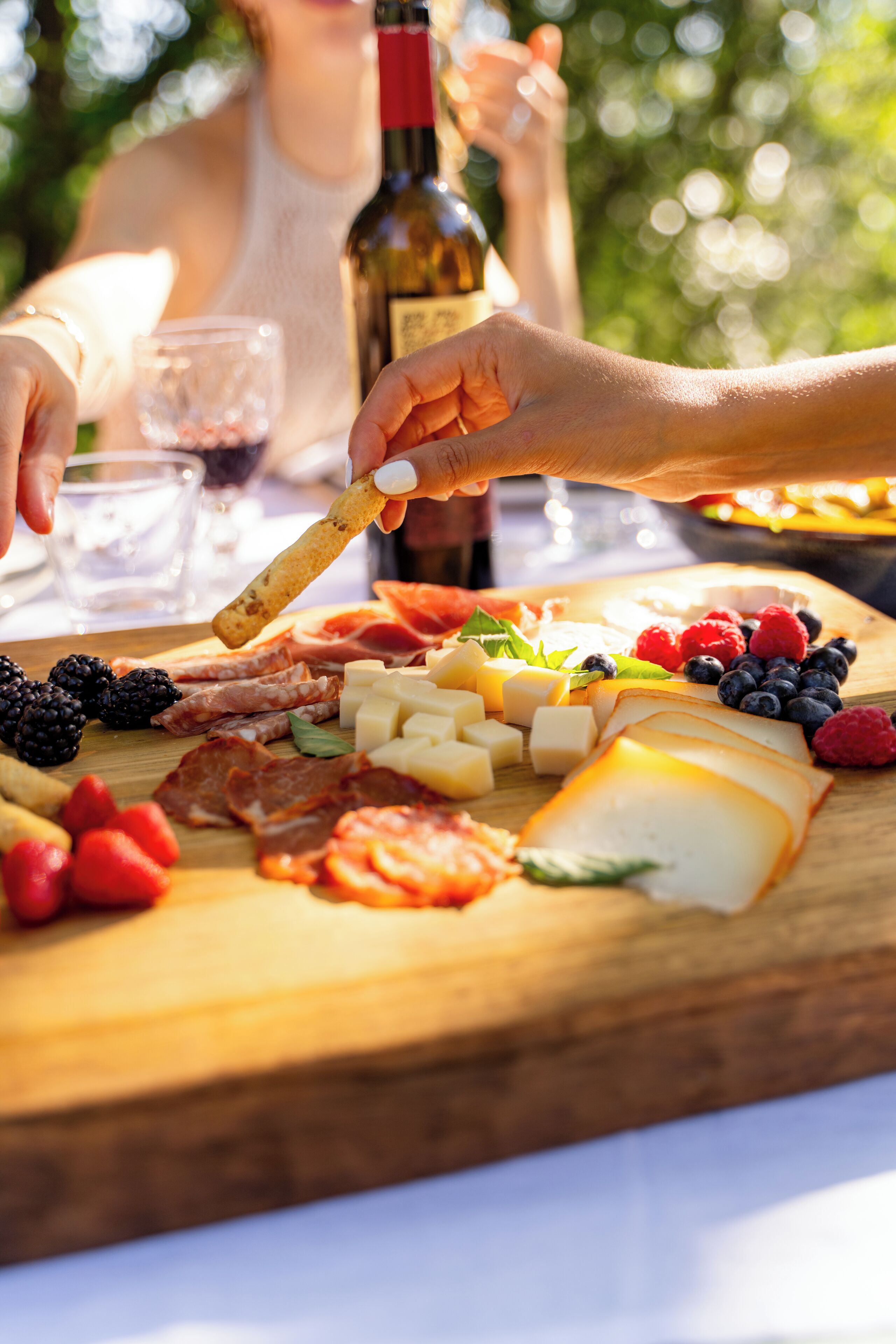 Una tabla de madera con varios quesos, frutas y embutidos.