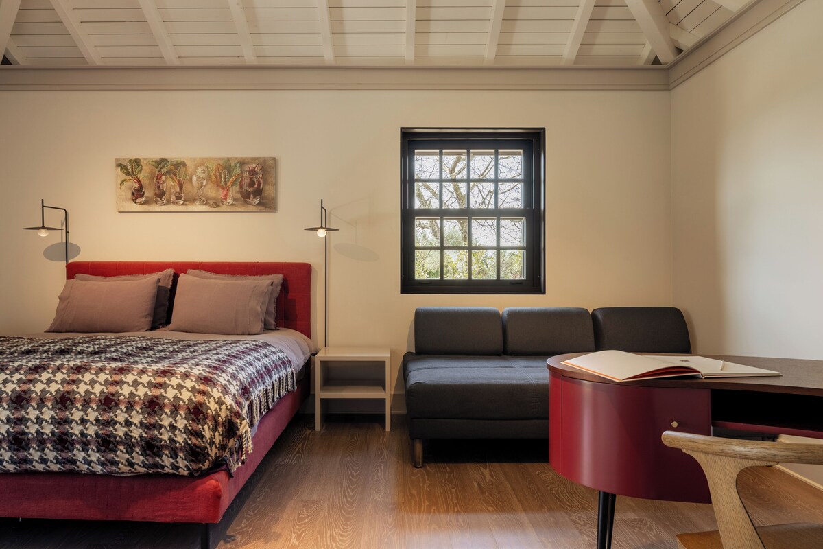 A bedroom with a bed, a sofa, a desk, and a window.