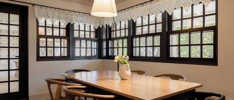 A dining area with a wooden table, chairs, lace curtains, and a hanging light fixture.