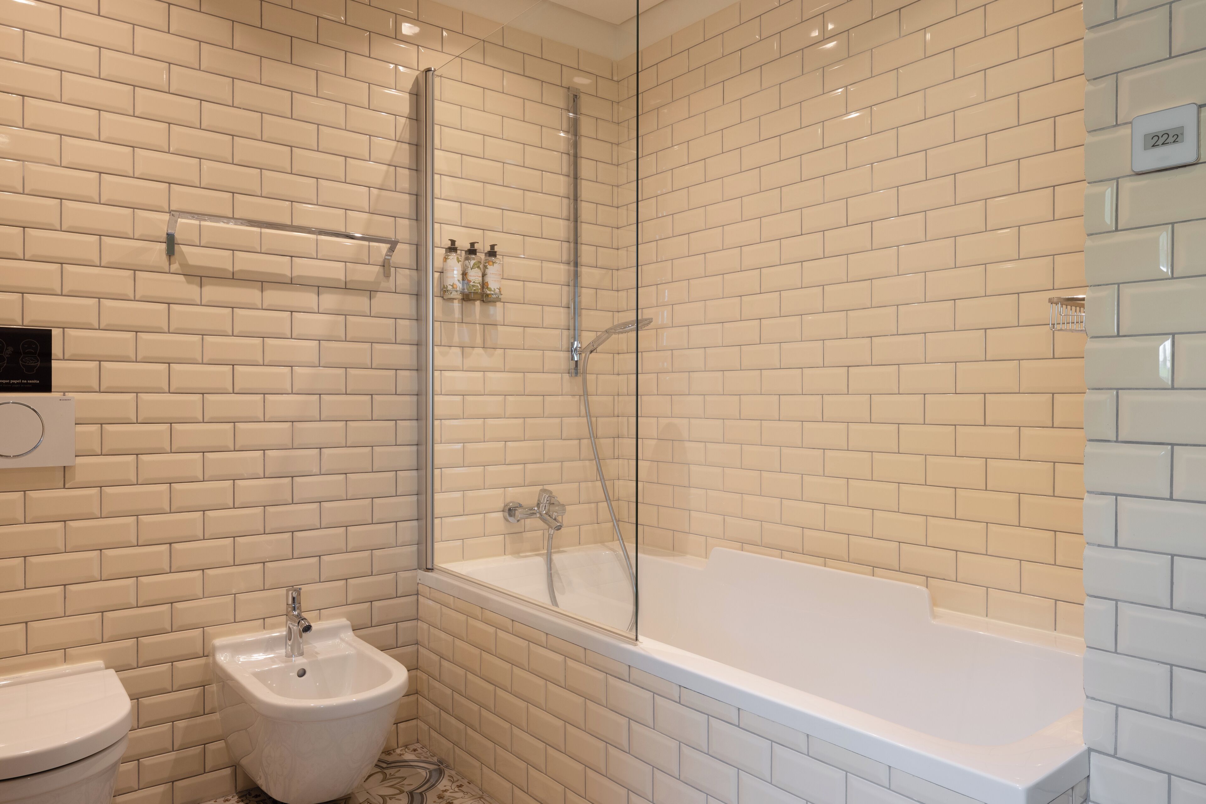 A modern bathroom with white subway tiles, a glass-enclosed shower, a white bathtub, and a bidet.
