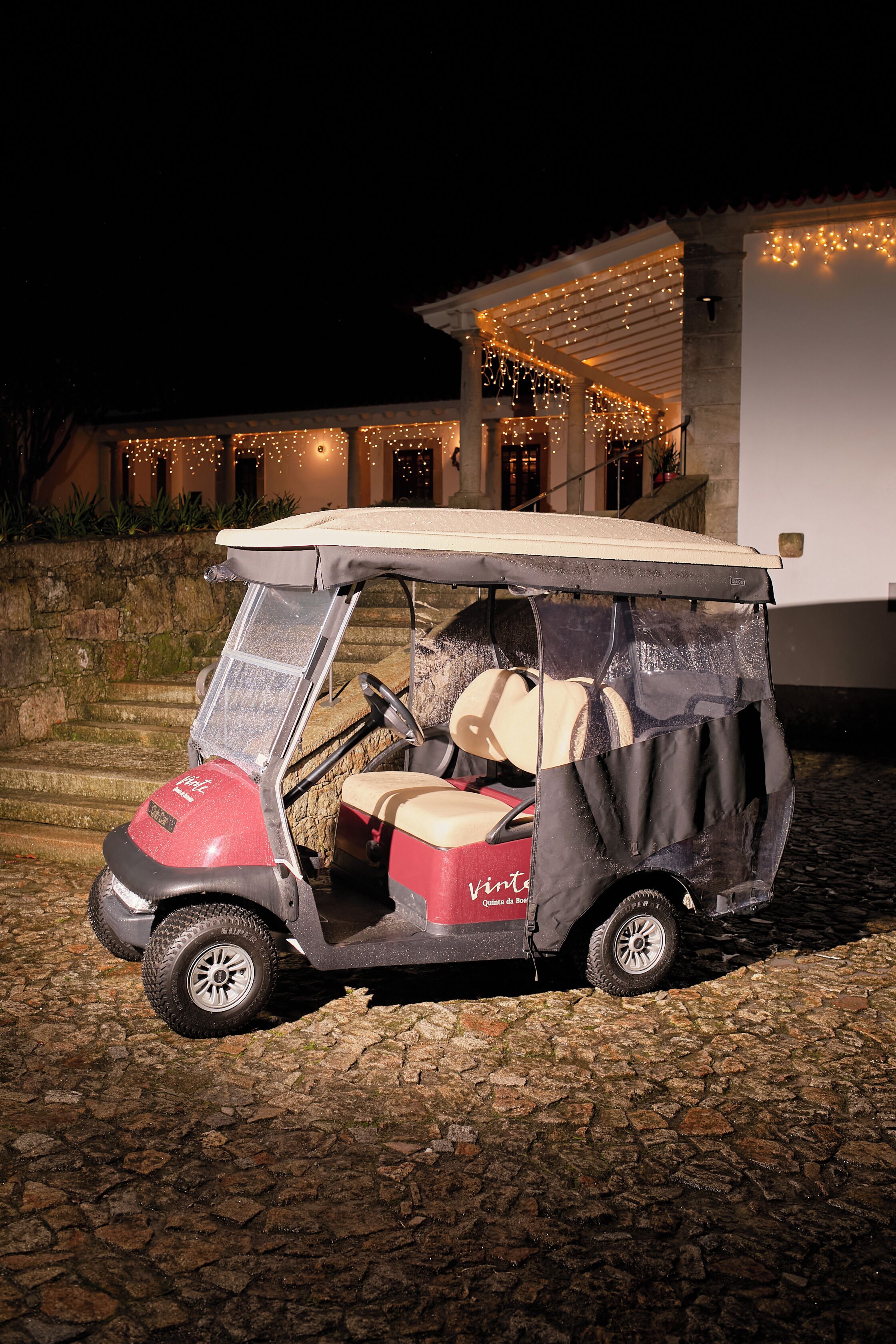 A golf cart parked on cobblestone ground in front of a building with string lights.