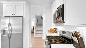 A modern kitchen with white cabinetry, stainless steel appliances, and a wooden cutting board on the countertop. - Beautiful 4 bedroom home with a pool! (Saint Simons Island)