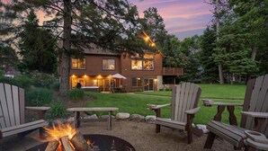 Une cabane en rondins avec un foyer et des fauteuils Adirondack dans la cour.