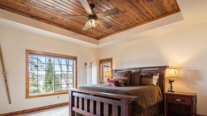 Une chambre avec un plafond en bois, une grande fenêtre, un lit avec une tête de lit et une table de chevet avec une lampe.