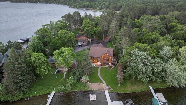 Vue aérienne d’une propriété au bord d’un lac, avec une grande maison entourée d’arbres denses, une jetée et un bateau.