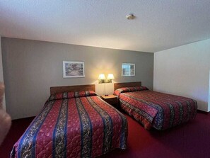 Hotellihuone, jossa on kaksi erillistä sänkyä, yöpöytä valaisimineen sekä kaksi kehystettyä kuvaa seinällä.