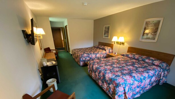 A hotel room with two beds, a desk, a chair, a trash bin, and two wall-mounted lamps. - Boulder Bear Motor Lodge (Boulder Junction)