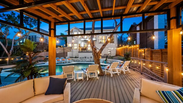 A wooden deck with lounge chairs and a pool, overlooking a house with string lights.