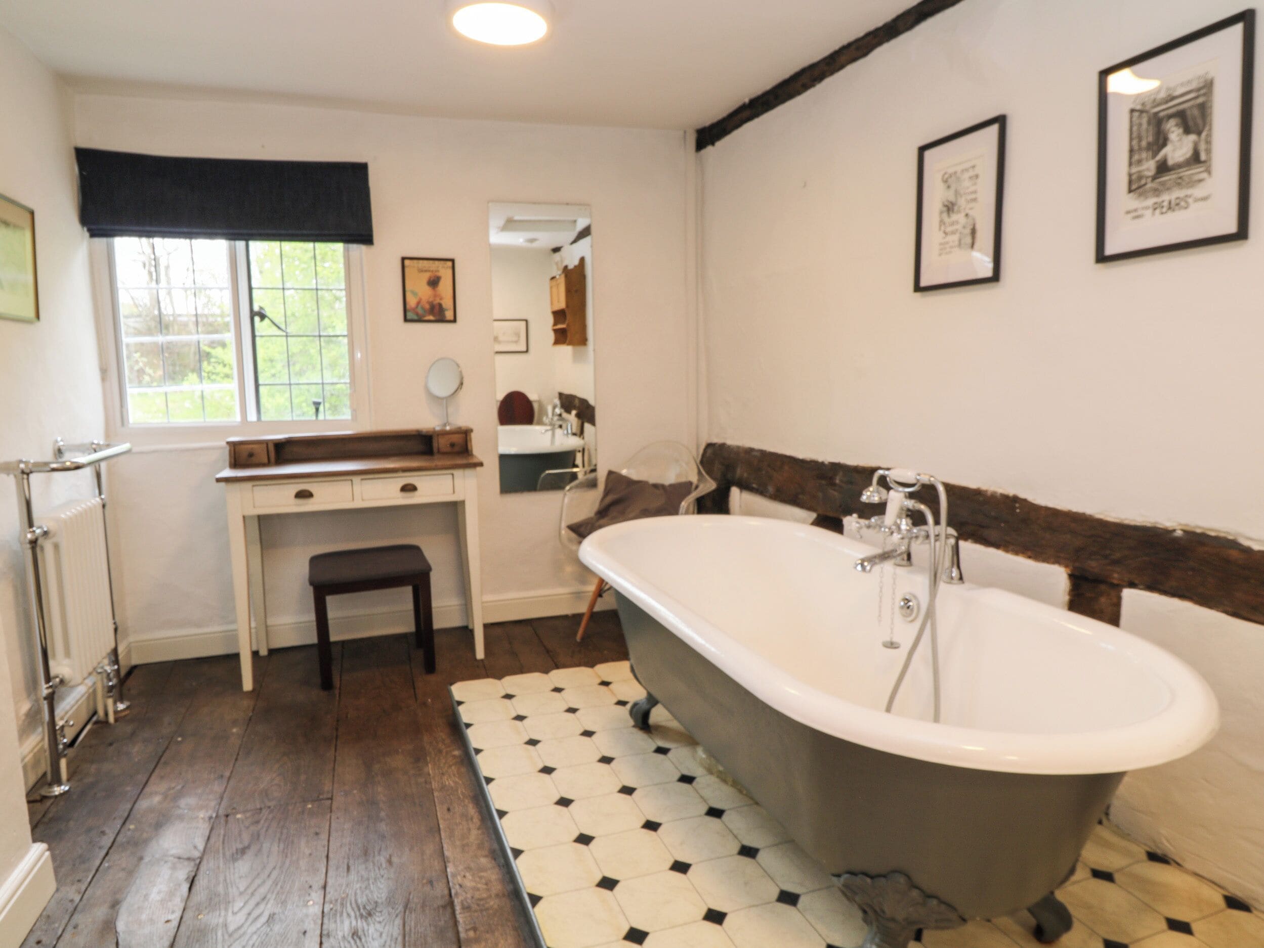 A bathroom with a freestanding bathtub, a vanity with a mirror, and a window with a view of greenery.