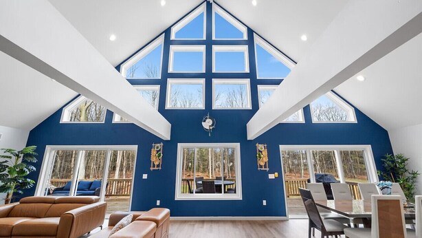 A spacious living room with a high ceiling, large windows, and a view of the outdoors.