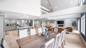 A spacious open-plan living area with a dining table, sofas, and a kitchen in the background.