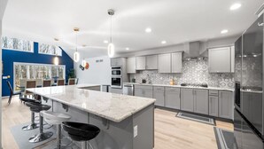 A modern kitchen with grey cabinets, a large island with bar stools, and a hexagonal backsplash.