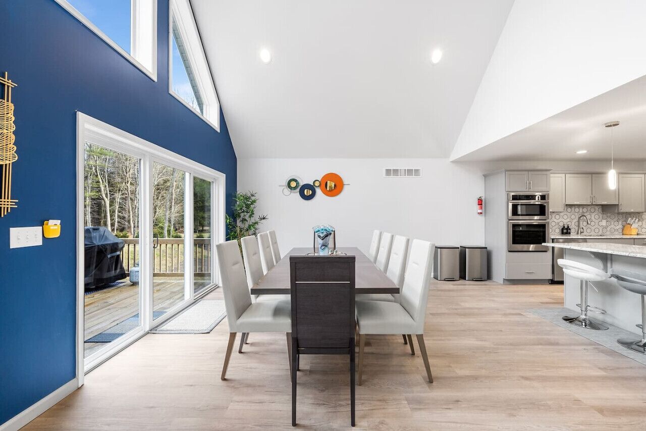 A modern kitchen with stainless steel appliances, a dining area with a long table and chairs, and a blue accent wall.