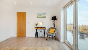 Une chambre moderne avec une porte en bois, un bureau avec une lampe, une chaise avec un coussin et une grande fenêtre.