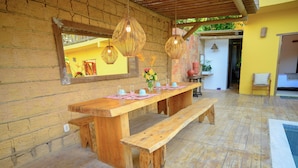 A wooden dining table with benches, hanging wicker lamps, and a large mirror on a brick wall. - Villa Beija Flôr (Porto Seguro)