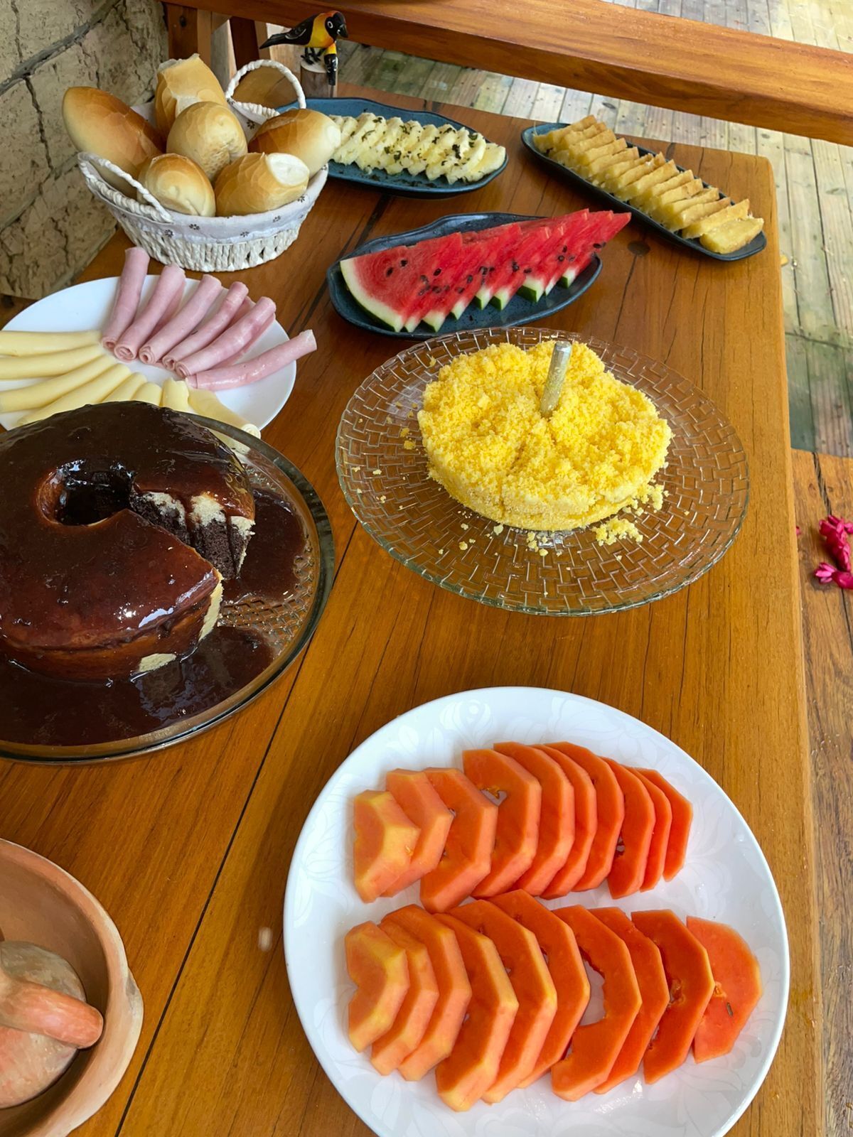 Ett träbord med olika sorters mat, inklusive bröd, skinka, vattenmelon och en chokladtårta.