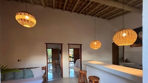 A modern interior with a wooden bench, a bar area with stools, and hanging wicker lamps. - Villa Beija Flôr (Porto Seguro)