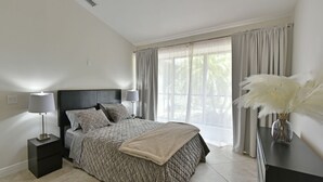 A bedroom with a bed, nightstands, a dresser, and a window with curtains.