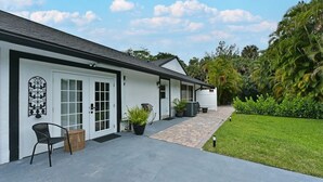 A white building with a garage door, a paved walkway, and a small garden area with potted plants.