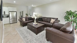 A modern living room with a brown leather sofa set, a dark wooden coffee table, and a patterned rug.