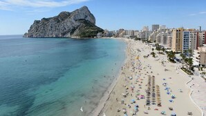 Una playa con un promontorio rocoso al fondo, una orilla arenosa y una hilera de edificios a lo largo de la costa.