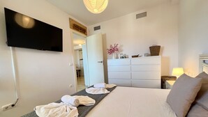 Una habitación de hotel con una cama, un televisor montado en la pared, un aparador y una lámpara.