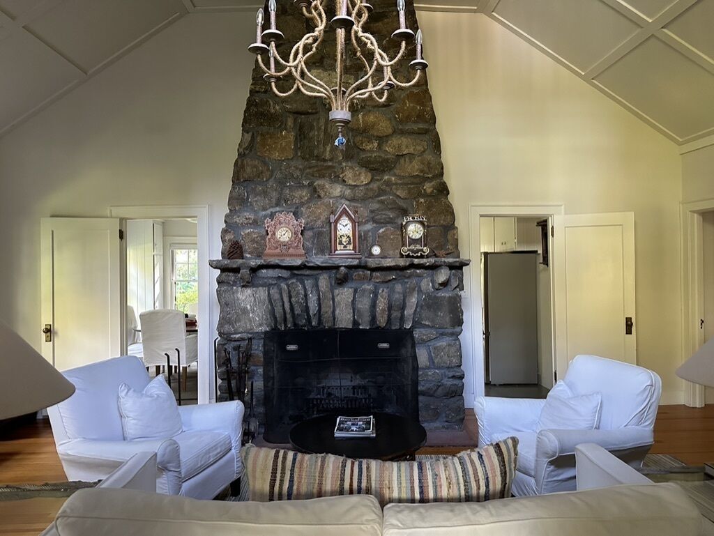 Ein Wohnzimmer mit Kamin aus Stein, weißen Sofas und einer Kristallleuchter.