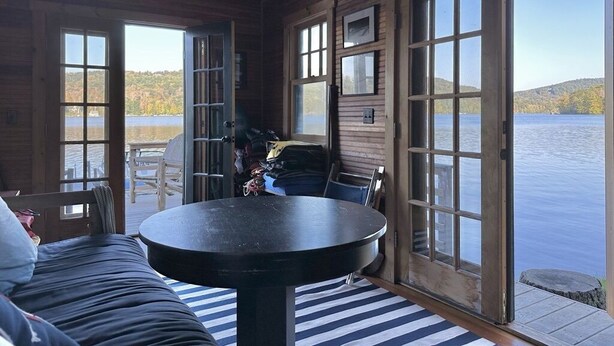 A cabin with a large window overlooking a lake, a round table, and a sofa. - LAKE GARFIELD WATERFRONT HOME AND BOATHOUSE (Monterey)