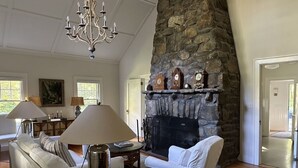 A living room with a stone fireplace, white sofas, a chandelier, and a coffee table. - LAKE GARFIELD WATERFRONT HOME AND BOATHOUSE (Monterey)