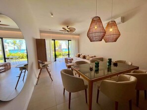 A modern living room with a glass dining table, beige sofas, and a view of the ocean.