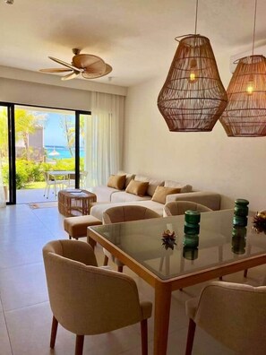 A modern living room with a glass dining table, beige sofas, and a ceiling fan.